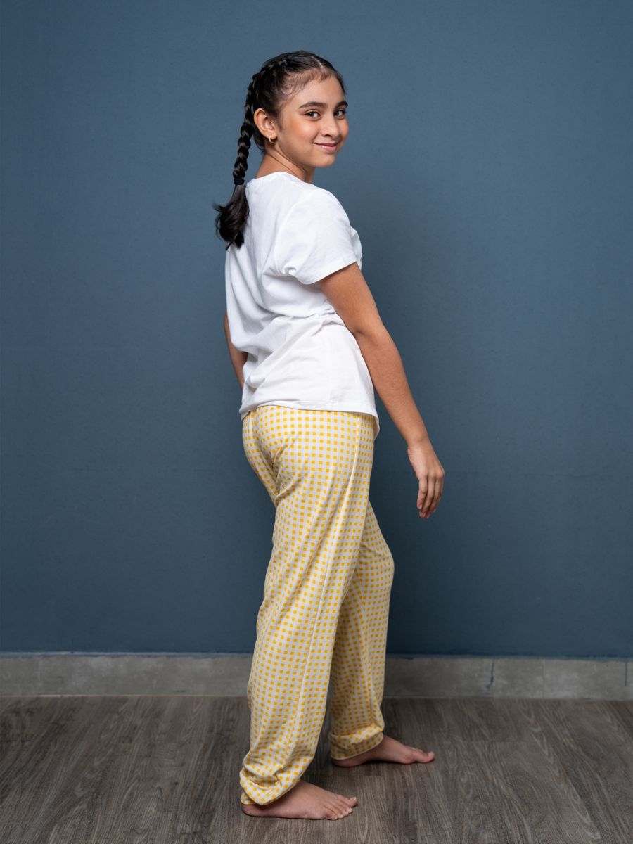 Woman wearing a white shirt and yellow checkered pants against a blue wall.