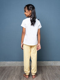 Child wearing a white shirt and yellow checkered pants against a blue wall.