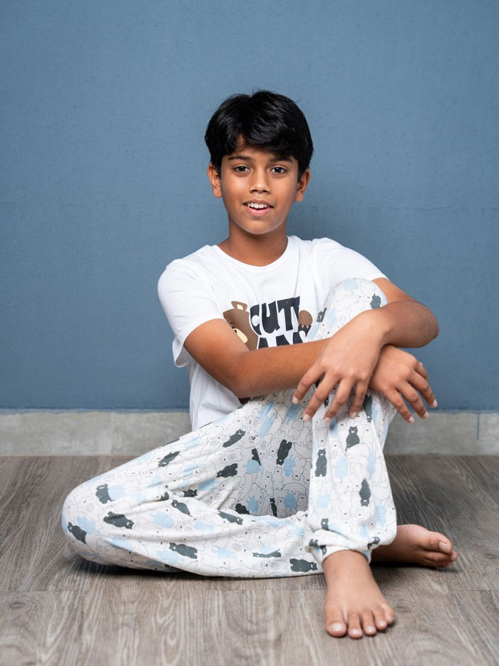 Child wearing a white t-shirt with graphics and light-colored pants sitting on a wooden floor against a blue wall.