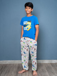 Young boy wearing a blue t-shirt with a graphic design and patterned pajama pants against a gray wall.