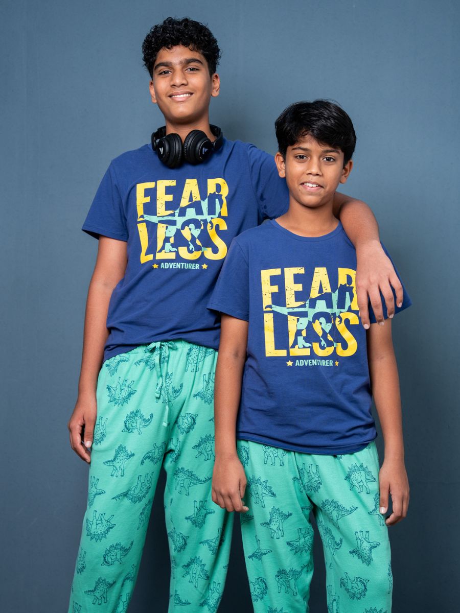 Two children wearing matching blue t-shirts with 'FEAR LESS' text and teal pants against a gray background.
