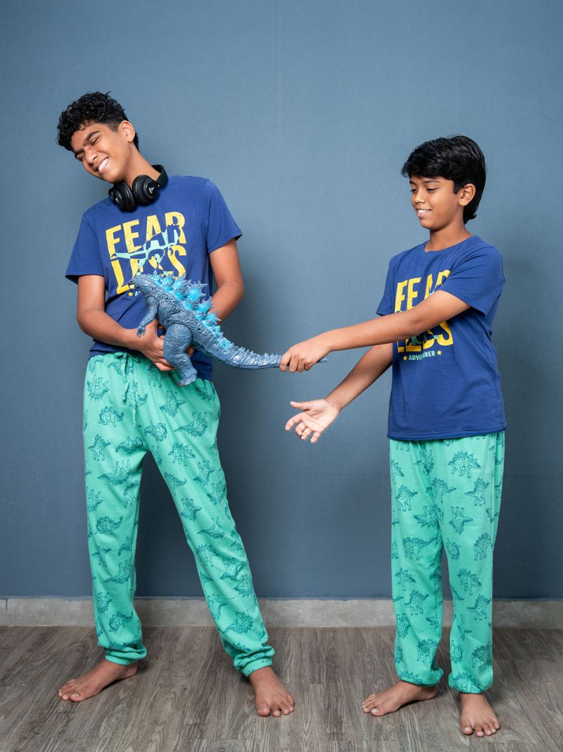 Two children wearing matching pajama sets wit (King of Dinosaurs) shirts against a gray background.