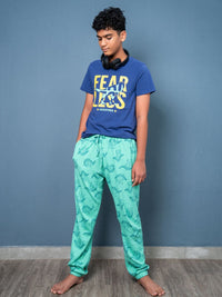 Person wearing a blue t-shirt with 'FEAR LESS' text and green patterned pants against a gray wall.