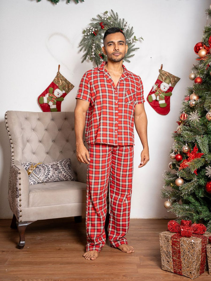 Man wearing red plaid pajamas standing in a festive room with Christmas decorations.
