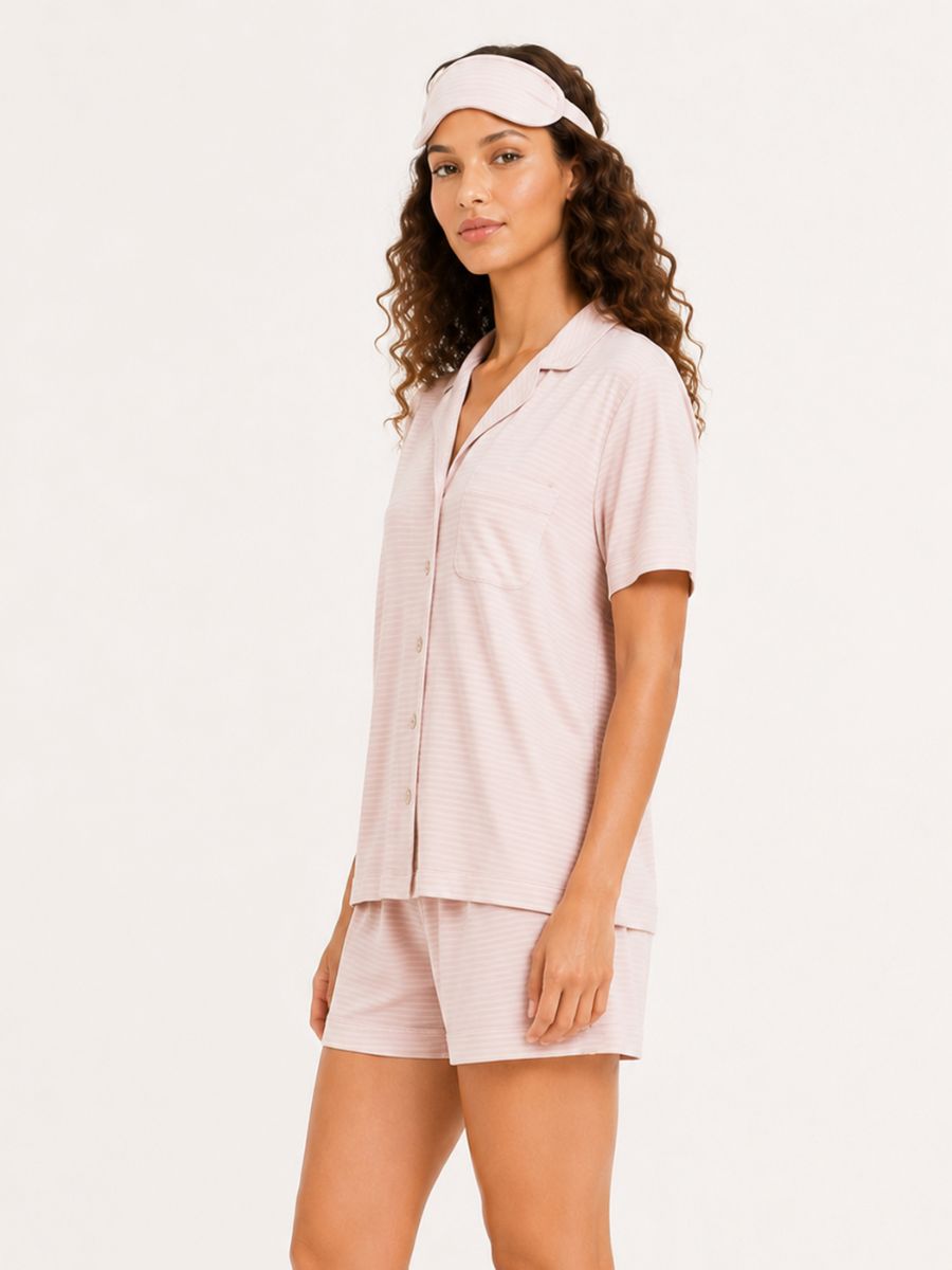 Woman wearing a light pink shirt and shorts set with a visor on a white background