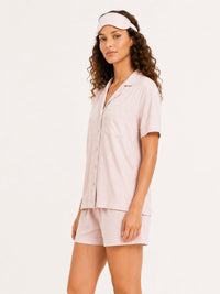 Woman wearing a light pink shirt and shorts set with a visor on a white background
