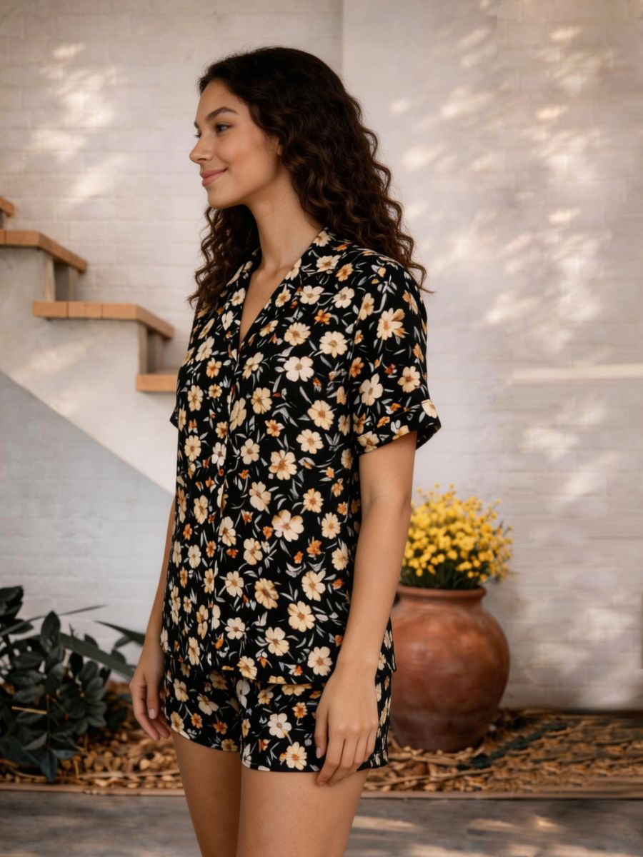 Woman wearing a black floral dress standing in a home setting with plants and a staircase.