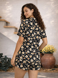 Woman wearing a floral romper standing in a home setting with plants.
