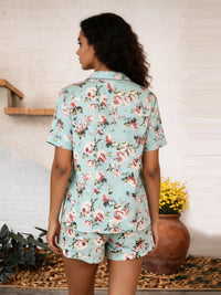 Woman wearing a floral pajama set with a white wall and plant in the background