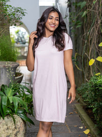 Woman in a light purple dress standing outdoors with greenery around