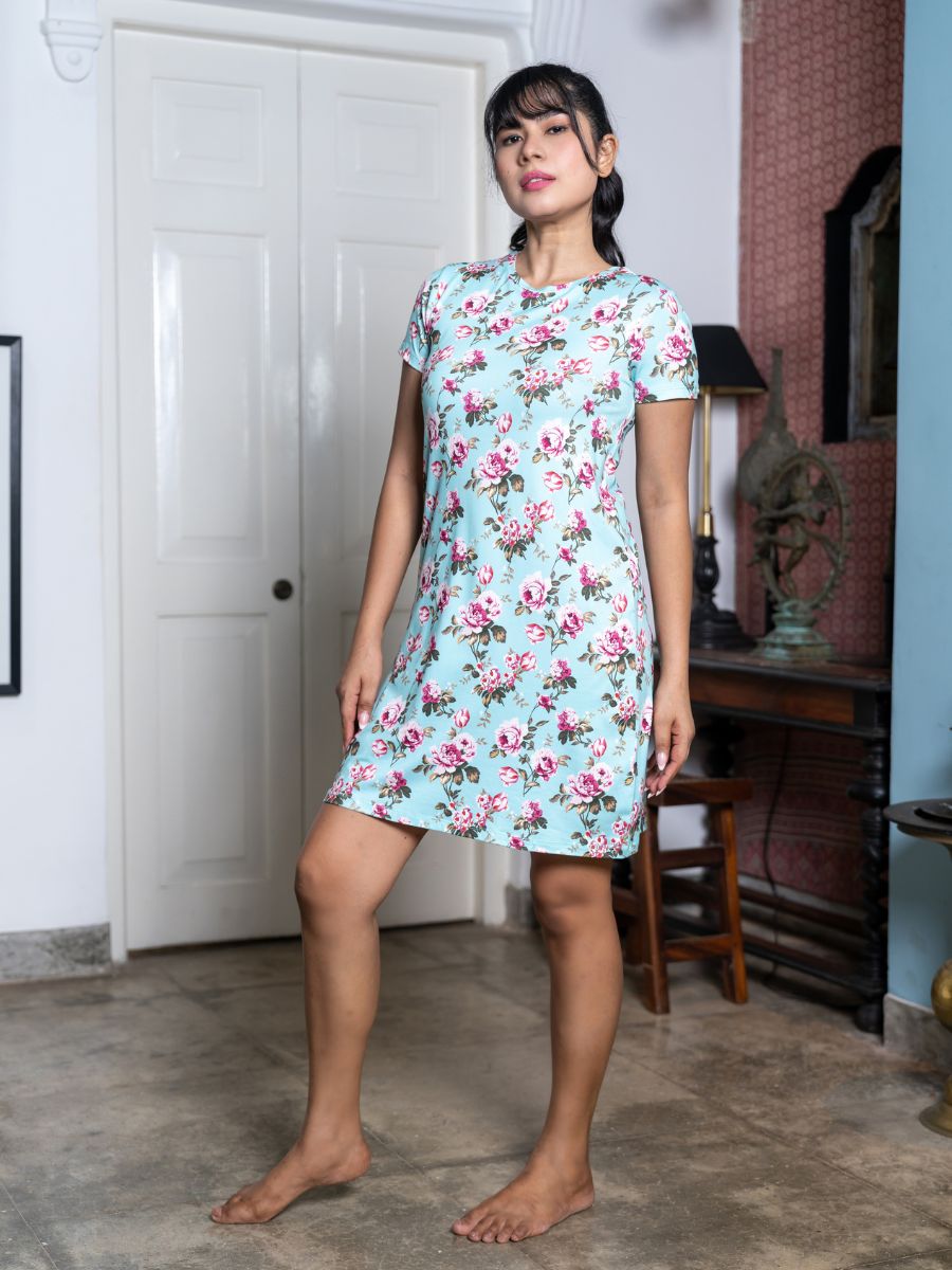 Woman wearing a floral dress standing in a room with a white door and wooden furniture.