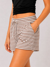 A person wearing striped lounge shorts with a drawstring waist and side pockets, paired with a black cropped top, against a light gray studio background.