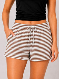 A person wearing striped lounge shorts with a drawstring waist and side pockets, paired with a black cropped top, against a light gray studio background.