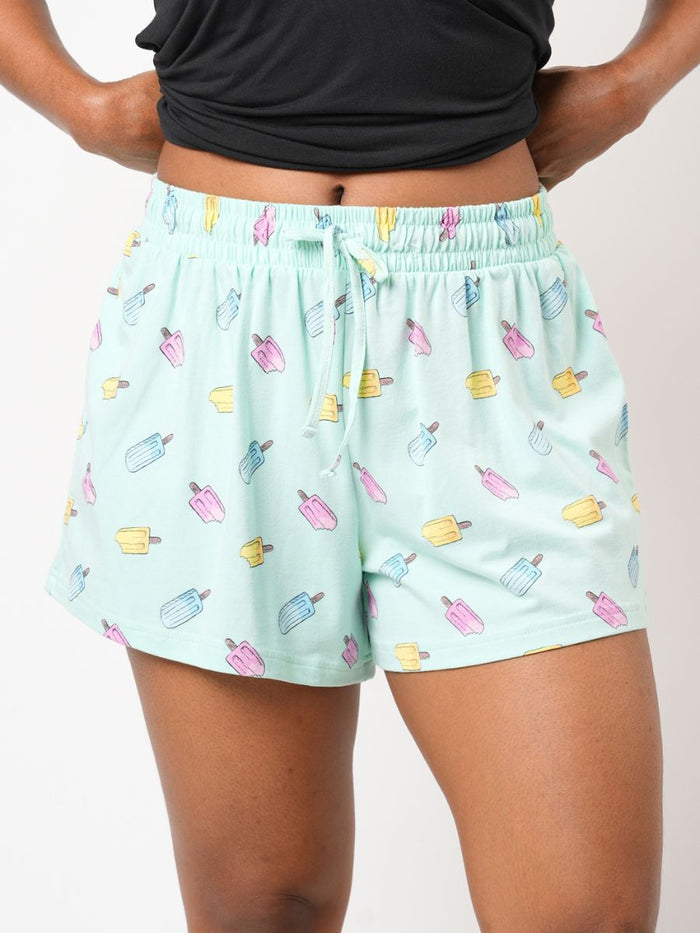 Person wearing light blue shorts with ice cream pattern on a plain background