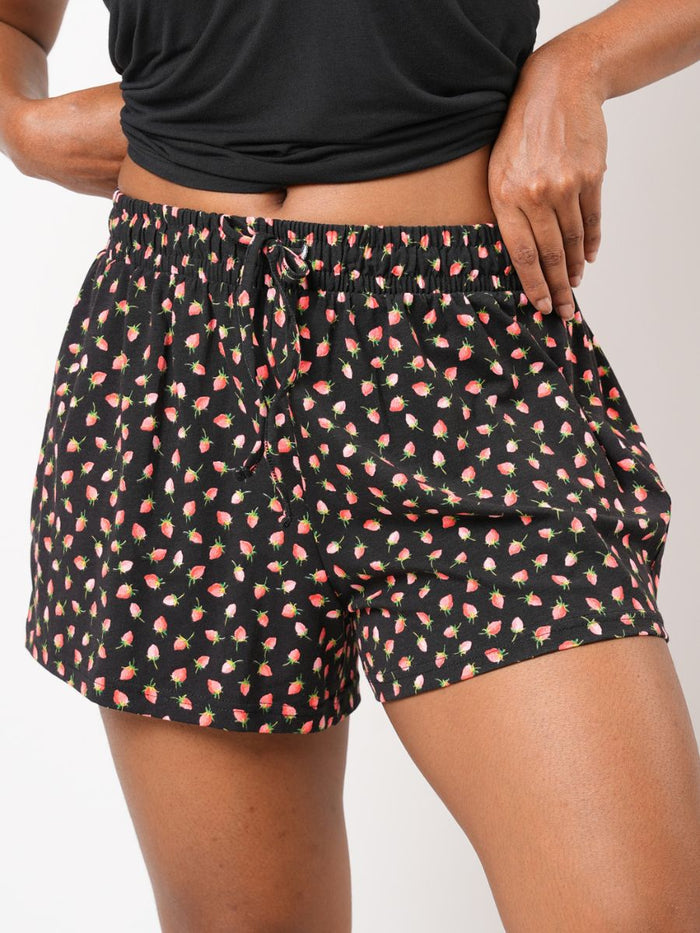Person wearing black shorts with pink floral pattern on a plain background