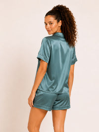 Woman wearing a teal satin pajama set on a beige background