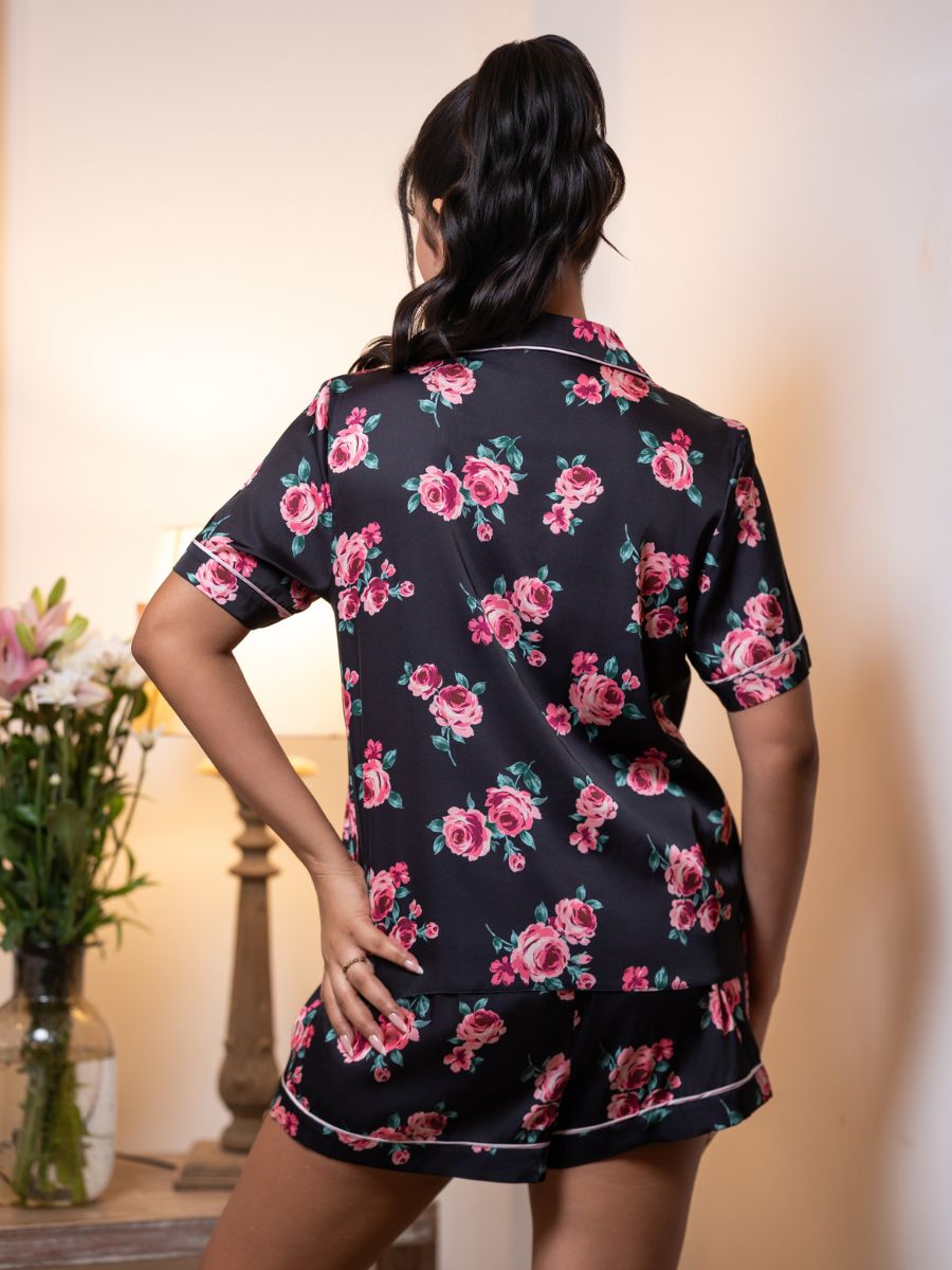 Woman wearing a black floral pajama set with pink roses and green leaves.