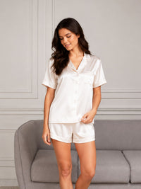Woman wearing a white satin pajama set standing in a room with a gray sofa.
