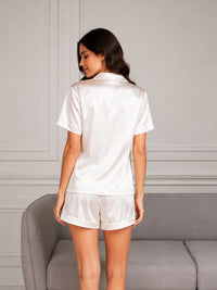 Woman wearing a white satin pajama set in a room with gray walls and furniture.