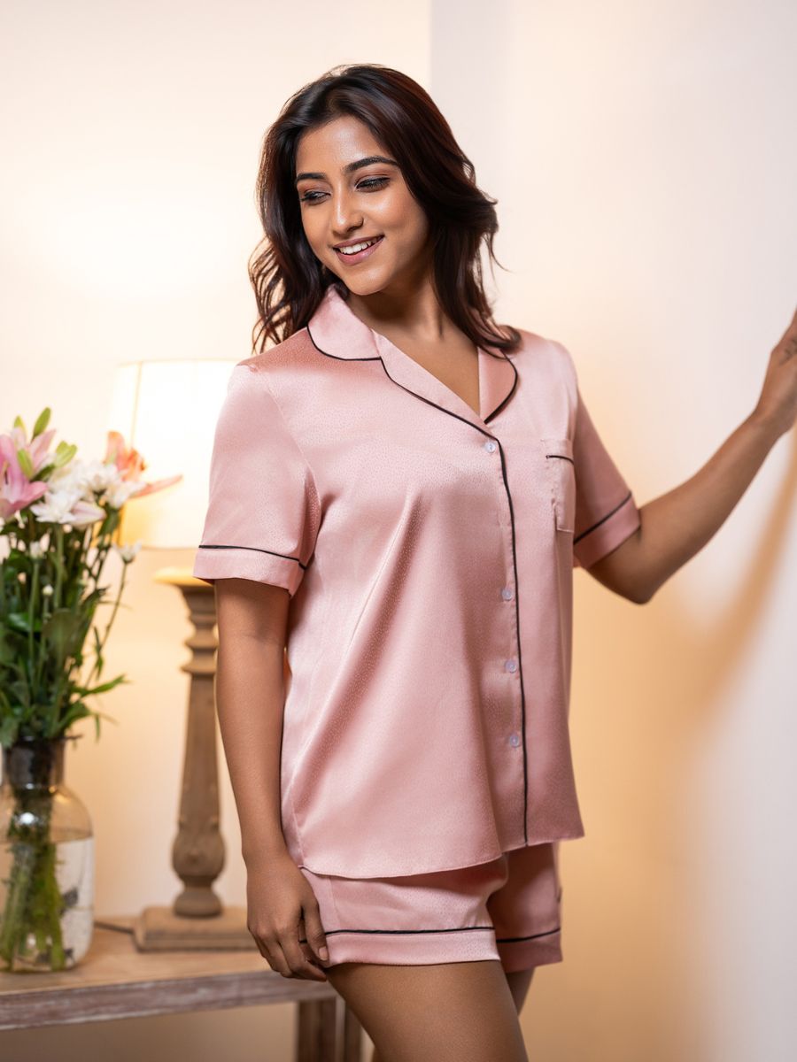 Woman wearing a pink satin pajama set in a softly lit room.