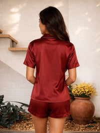Woman wearing a red satin outfit standing in a room with plants and a vase.