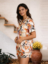 Woman wearing a floral pajama set standing in a home setting with plants and a vase.