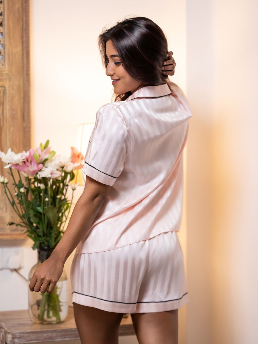 Woman in a white pajama set holding a vase of flowers indoors.