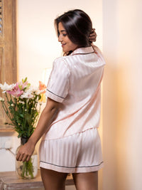 Woman in a white pajama set holding a vase of flowers indoors.