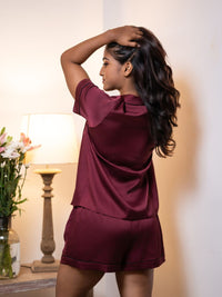 Woman wearing a burgundy outfit in a softly lit room with flowers and a lamp.