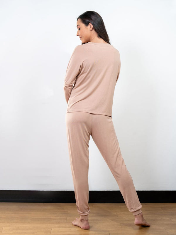 Woman wearing a beige loungewear set against a white wall.