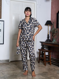 Woman wearing a floral pajama set in a room with a lamp and wooden furniture.