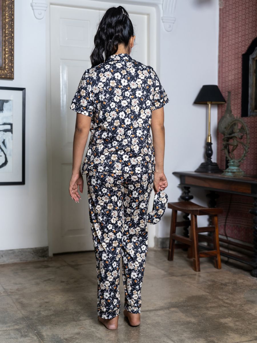 Woman wearing a floral outfit standing in a room with a lamp and framed pictures on the wall.
