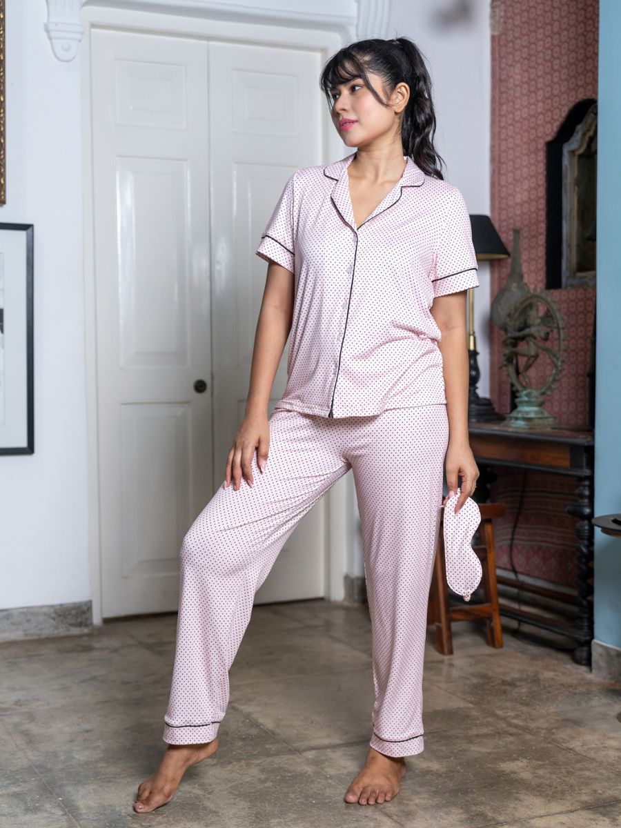 Woman wearing pink pajama set standing in a room with a white door and wooden furniture.