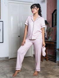 Woman wearing pink pajama set standing in a room with a white door and wooden furniture.