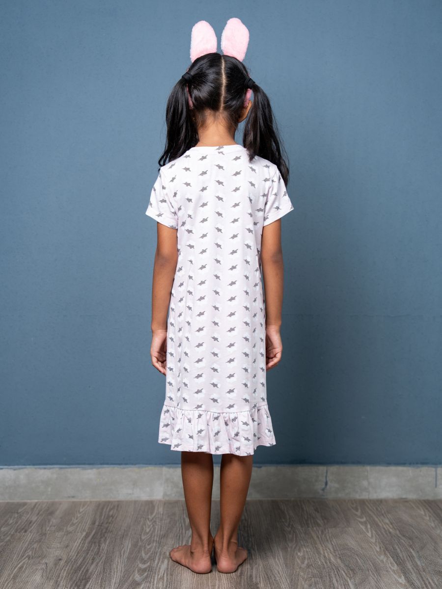Child wearing a white dress with small patterns and pink bunny ears against a blue wall.