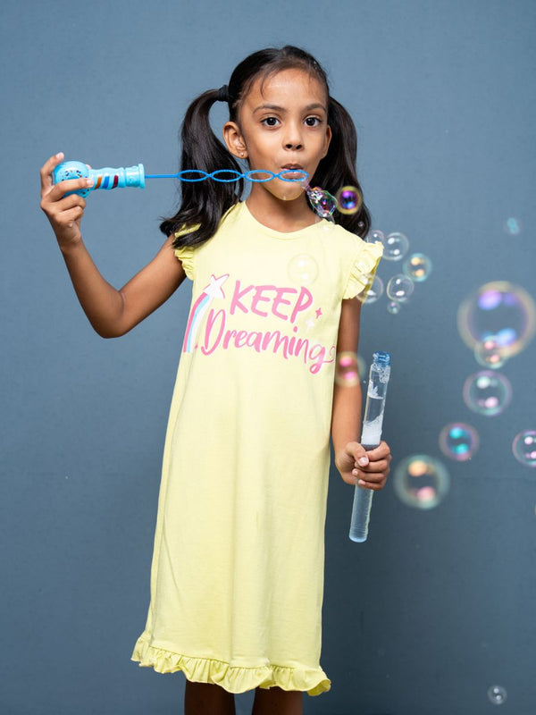 Girl blowing bubbles wearing a yellow nightgown with 'Keep Dreaming' text on a gray background