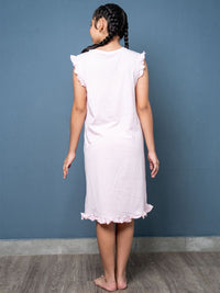 Young girl wearing a lilac dress with ruffled sleeves and hem against a blue wall.