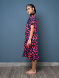 Girl wearing a pink and blue patterned dress against a blue wall.