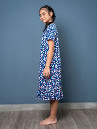 Young girl wearing a blue floral dress against a gray wall.