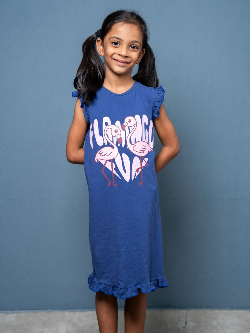 Young girl wearing a blue dress with flamingo design against a gray background
