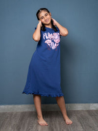Young girl wearing a blue nightgown with a pink design against a blue wall.