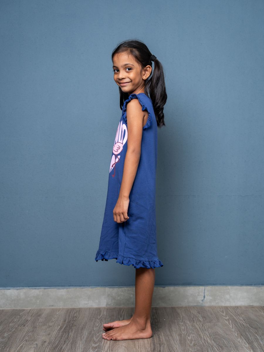 Young girl wearing a blue dress with a logo against a blue wall