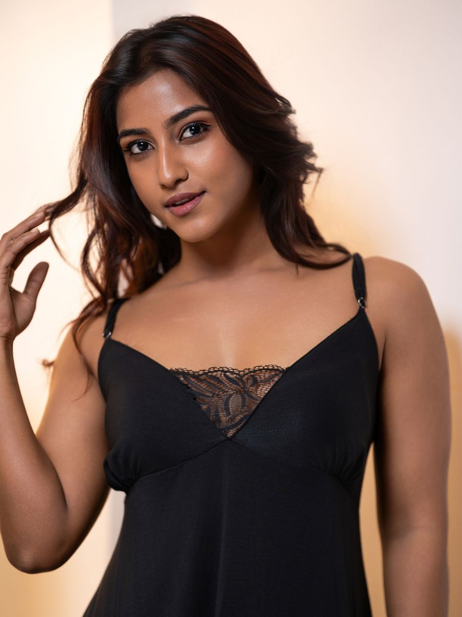 Woman wearing a black slip dress with lace details against a neutral background