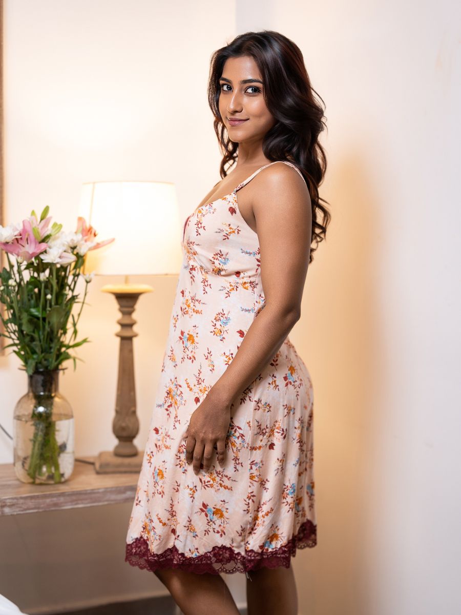 Woman wearing a floral dress standing indoors with a lamp and flowers in the background