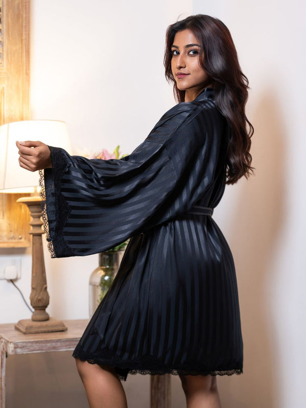 Woman wearing a black satin robe in a softly lit room.