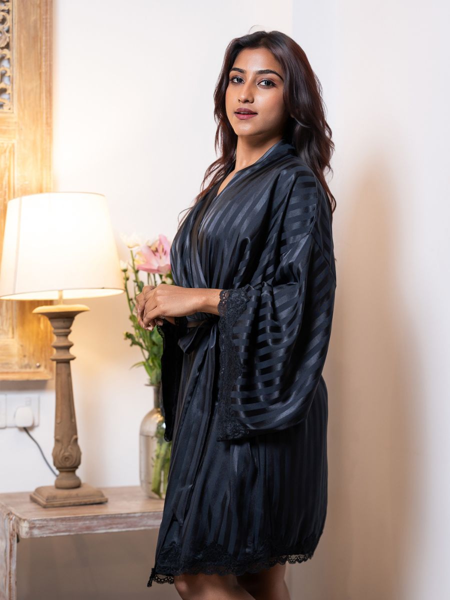 Woman wearing a black robe standing in a room with a lamp and decorative items.