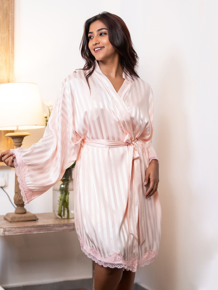 Woman wearing a light pink satin robe in a softly lit room.