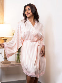 Woman wearing a light pink satin robe in a softly lit room.