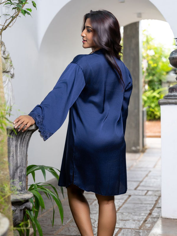 Woman wearing a blue dress standing in an outdoor setting with plants and arches.