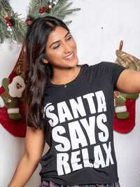 Woman wearing a black t-shirt with 'Santa Says Relax' text in front of Christmas stockings.